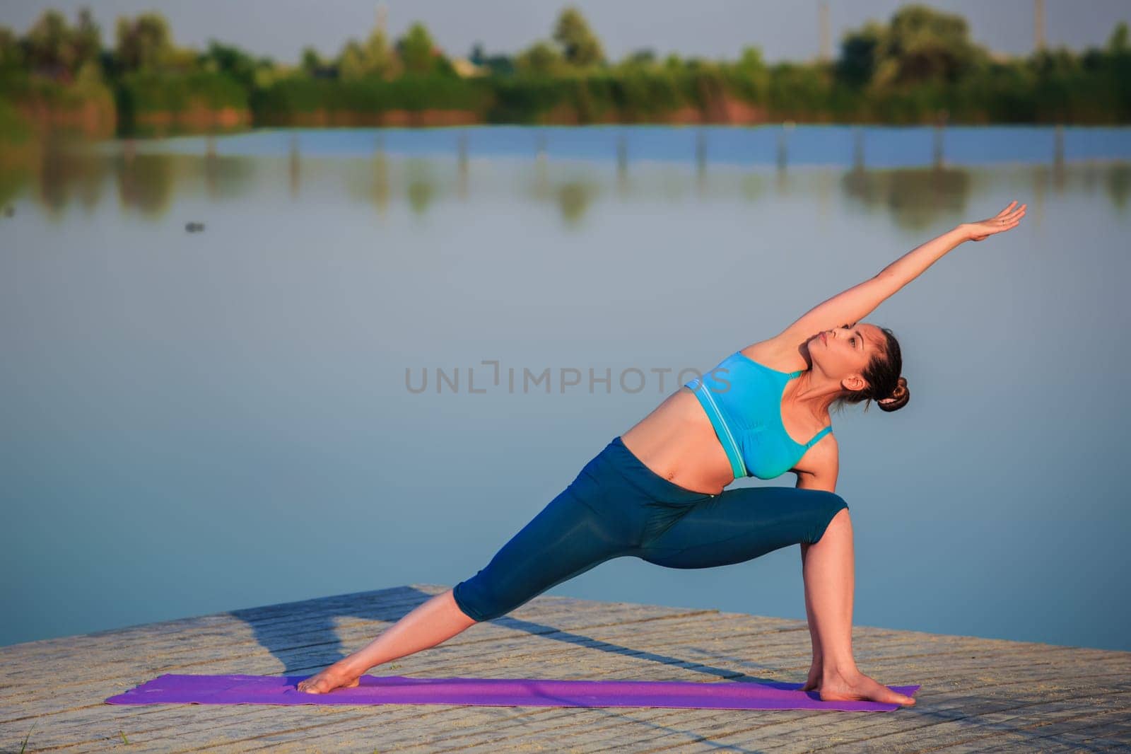 girl doing yoga exercises on the river bank at sunset
