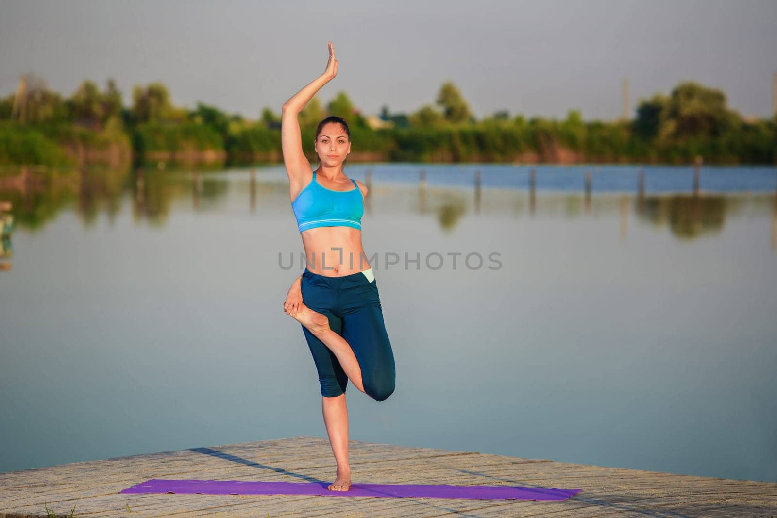 girl doing yoga exercises on the river bank at sunset