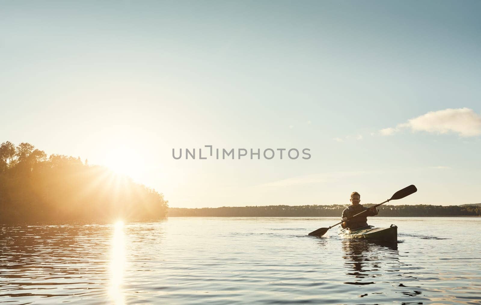Exploring the outdoors one paddle at a time. a young man kayaking on a lake outdoors. by YuriArcurs