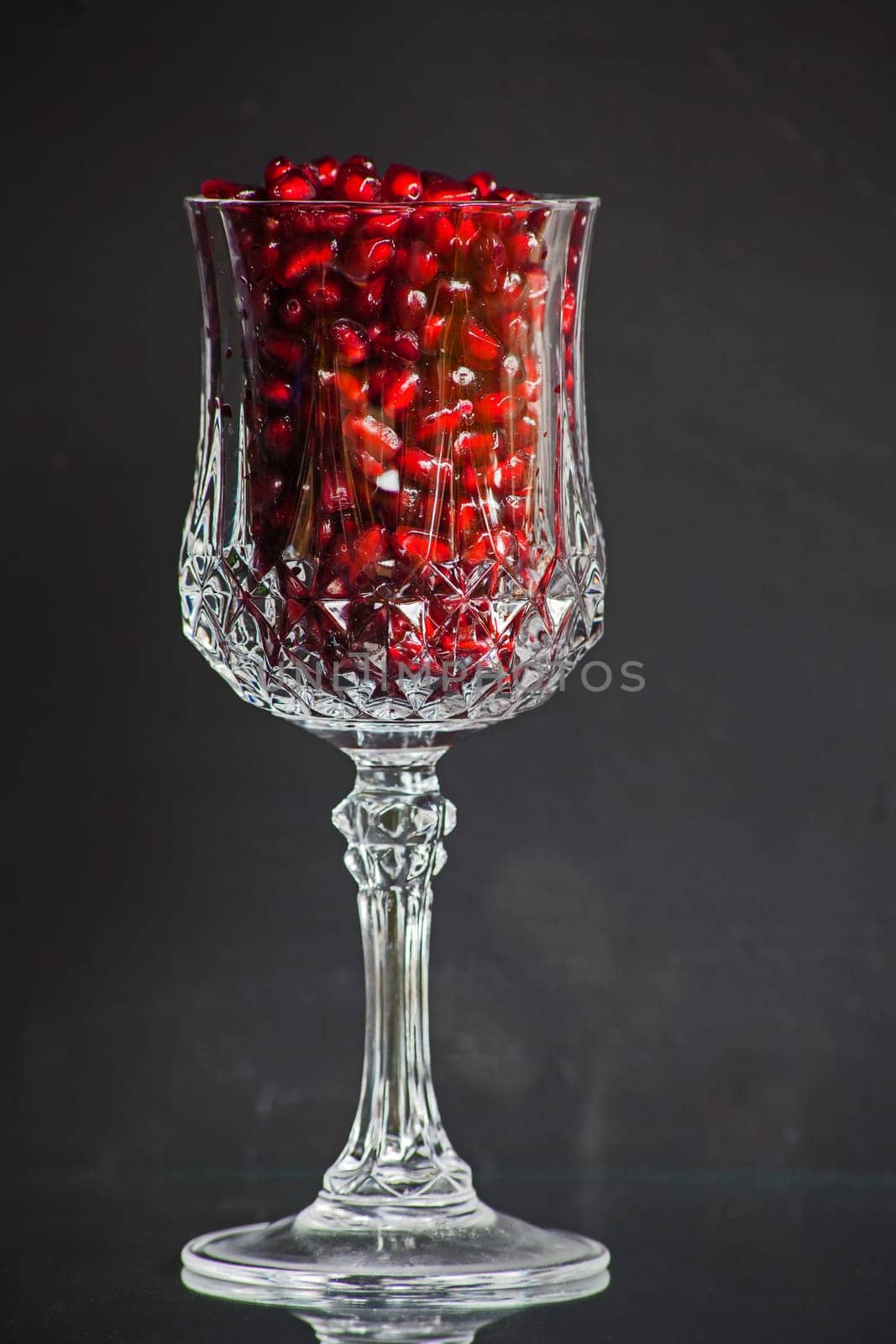 Still live of a single cut crystal glass filled with shiny pomegranitate seeds.