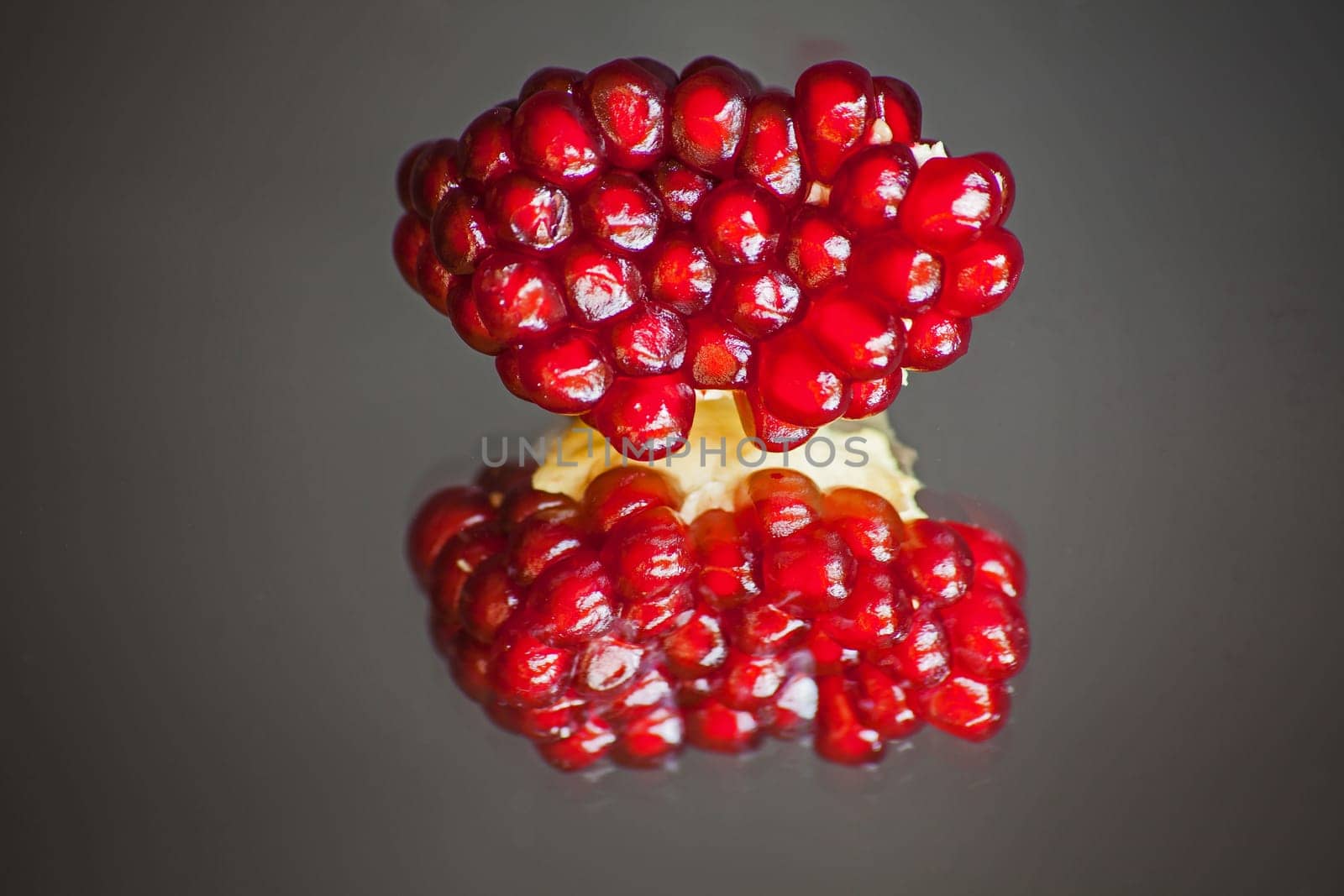 Ripe Pomegranate seeds in the fruit body reflected in glass, on a dark blurred background