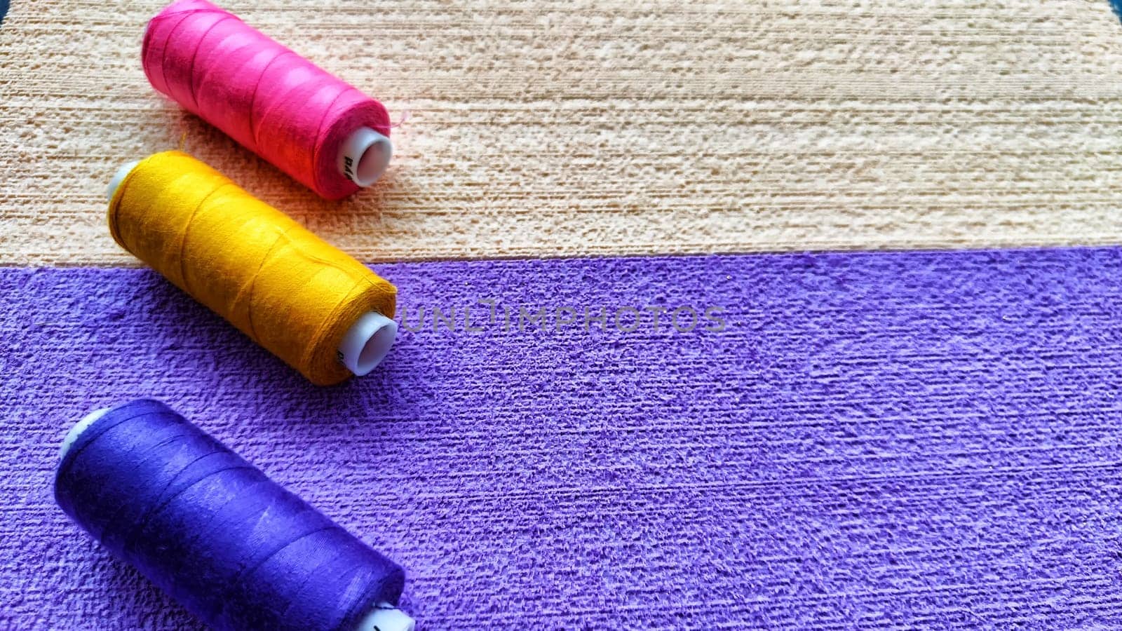 Abstract background with texture and frame with beige, lilac or purple velvet paper and colour pink, yellow, blue spools of thread with copy space
