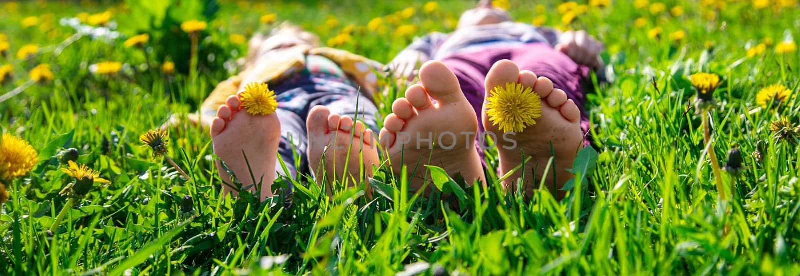 Child feet on the grass in the spring dandelions garden. Selective focus. by yanadjana