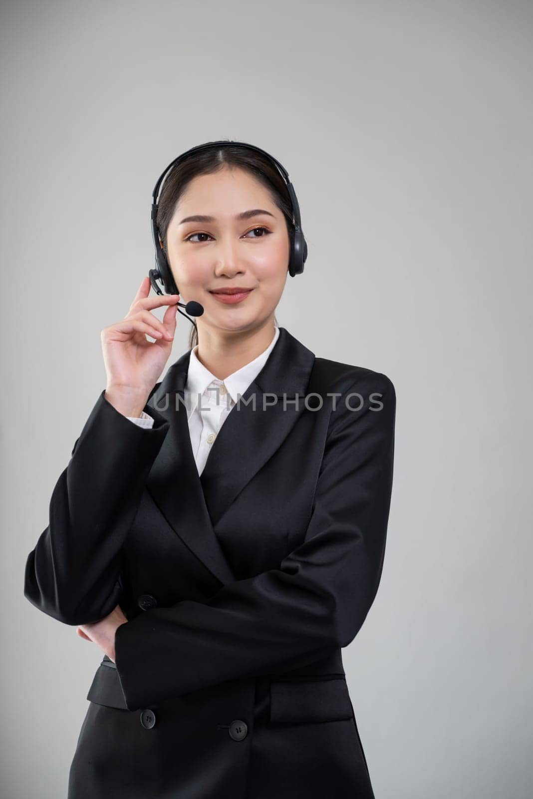 Attractive asian female call center operator with happy smile face advertises job opportunity on empty space, wearing a formal suit and headset on customizable isolated background. Enthusiastic