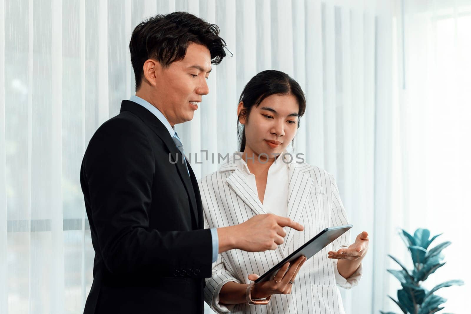 Manager advising guiding younger colleague with tablet in workplace. Couple businesspeople in formal wear working together on financial strategy as concept of teamwork and harmony in office.