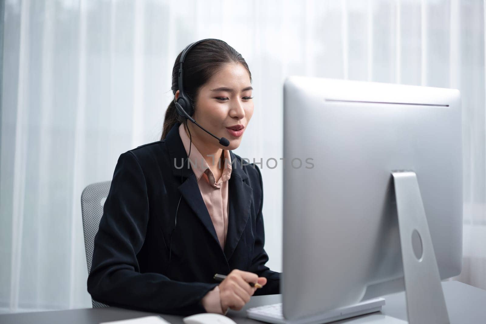 Asian call center with headset and microphone working on her laptop. Female operator provide exceptional customer service. Supportive call center agent helping customer on inquiry. Enthusiastic