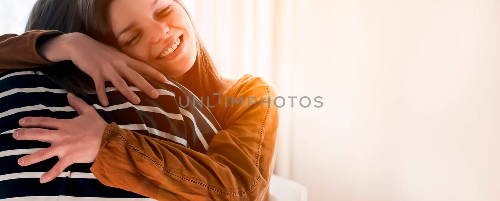 Two friends are embracing in the sun and happy to meet each other. Girls celebrate the holidays or anniversary and hug tightly and warm, feel an emotional connection and love, smiley face closeup.