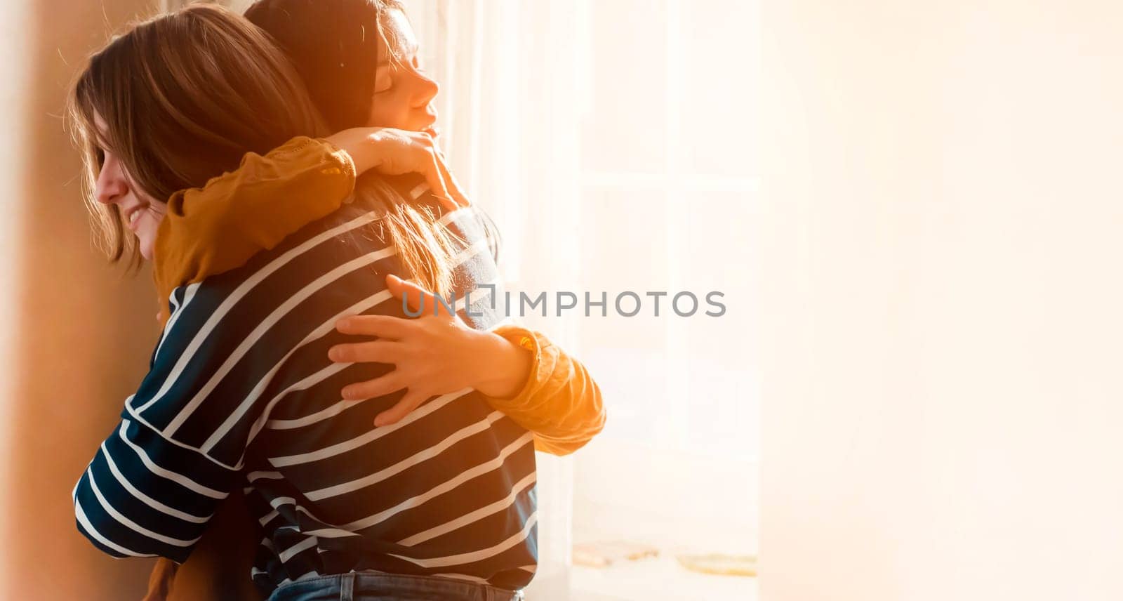 Two female friends of different ethnicity are embracing in the sun and happy to meet each other. Girls celebrate the holidays and hug tightly and warm, feel an emotional connection and love.