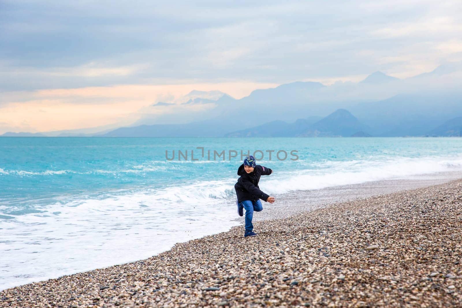 Boy running away from the wave. Storm in the Mediterranean Sea. Beautiful rocky shore with rolling waves. Turkiye, Antalya.