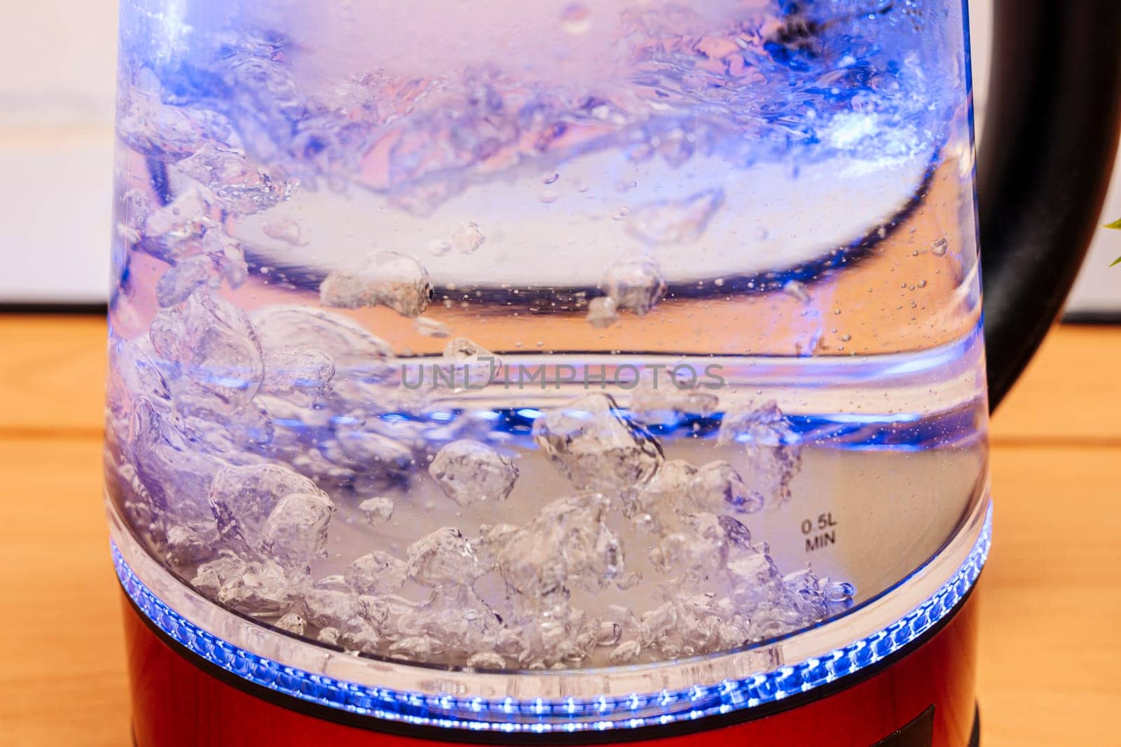 a new modern electric kettle made of red boiling glass in close-up with bubbling water and blue neon lighting. Boiling water and bubbles. Breakfast, afternoon tea