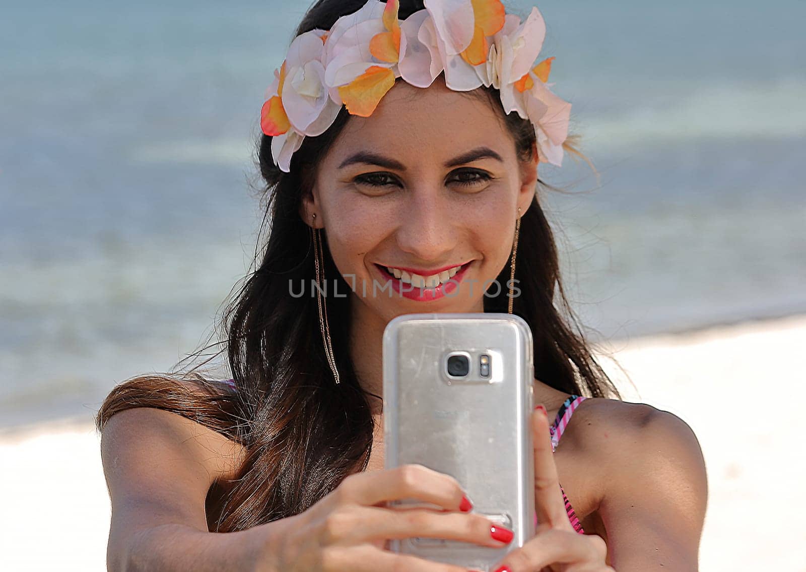 Smiling young woman taking selfie with smartphone on beach by Marcielito