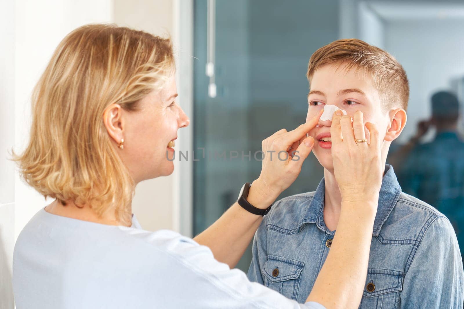 mom glues a patch to remove blackheads to her son. acne remover patch. teenage with nose band aid