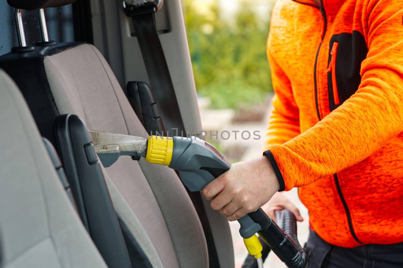 Handyman vacuuming car front textile seat with vacuum cleaner. man cleaning work Minivan.