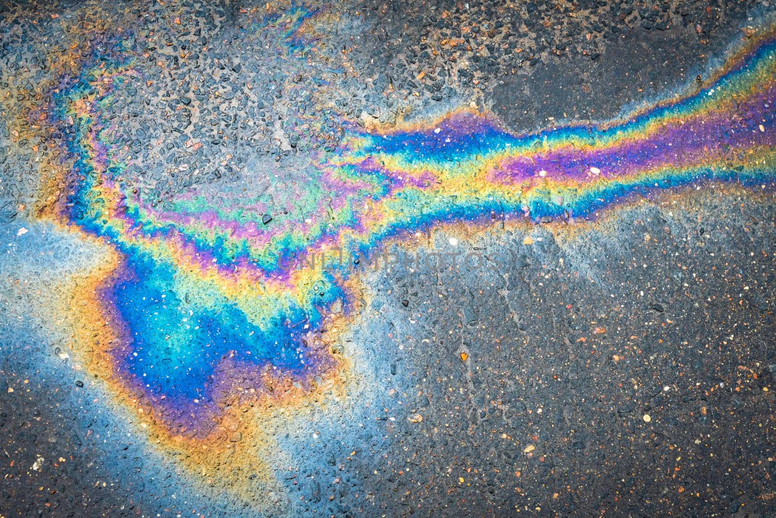 Oil stains from leaks in the car engine. Oil after rain makes spots with rainbow reflections refractive sun spectrum. Beautiful color mosaic, abstraction, ecology