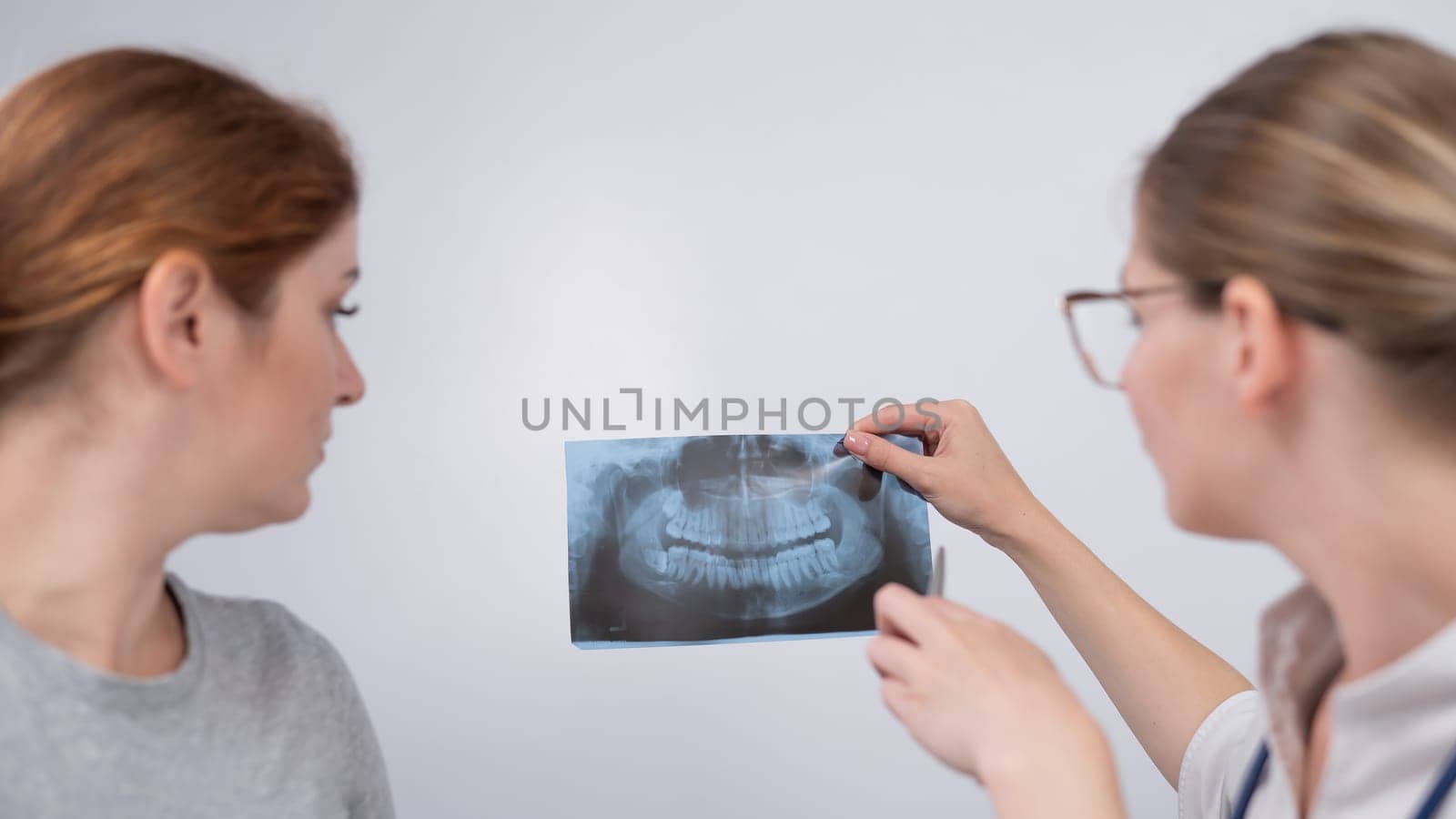 A woman doctor and a patient at the reception are discussing an x-ray of the jaw. by mrwed54