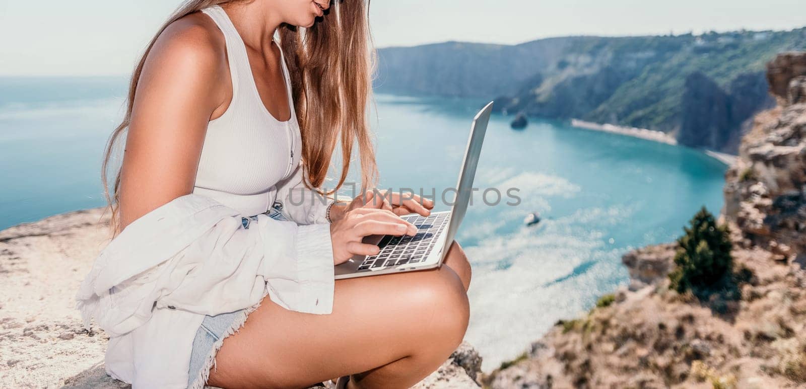 Digital nomad, Business woman working on laptop by the sea. Pretty lady typing on computer by the sea at sunset, makes a business transaction online from a distance. Freelance remote work on vacation