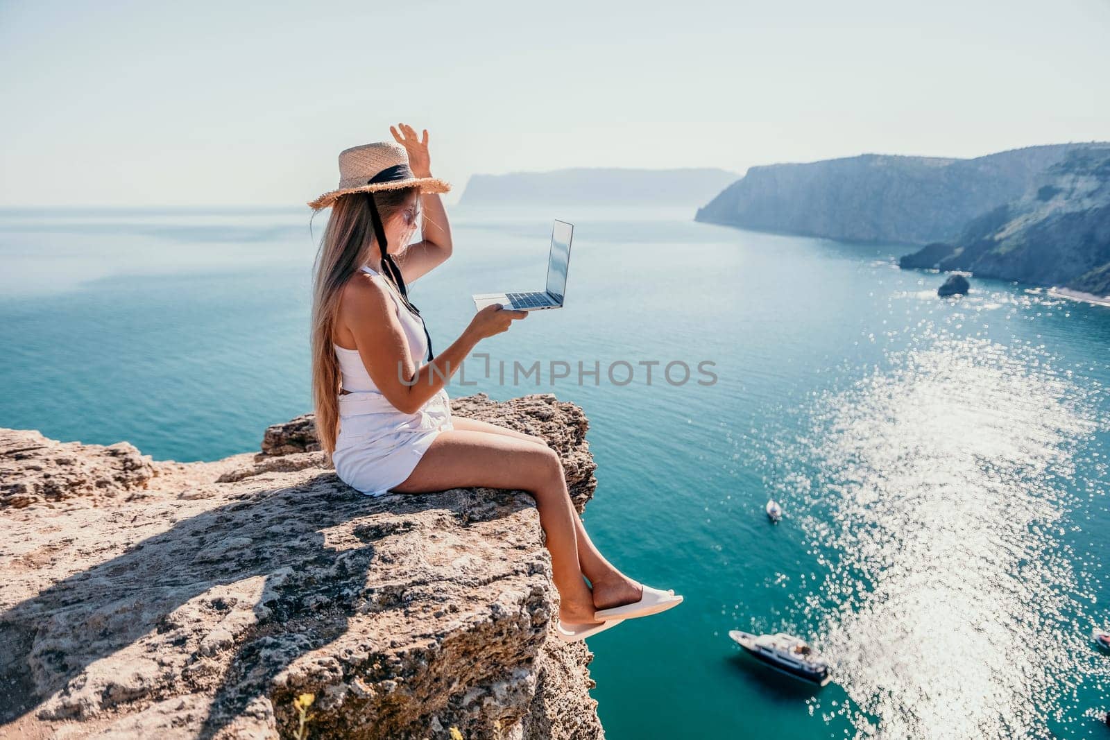 Woman laptop sea. Working remotely on seashore. Happy successful woman female freelancer in straw hat working on laptop by the sea at sunset. Freelance, remote work on vacation by panophotograph