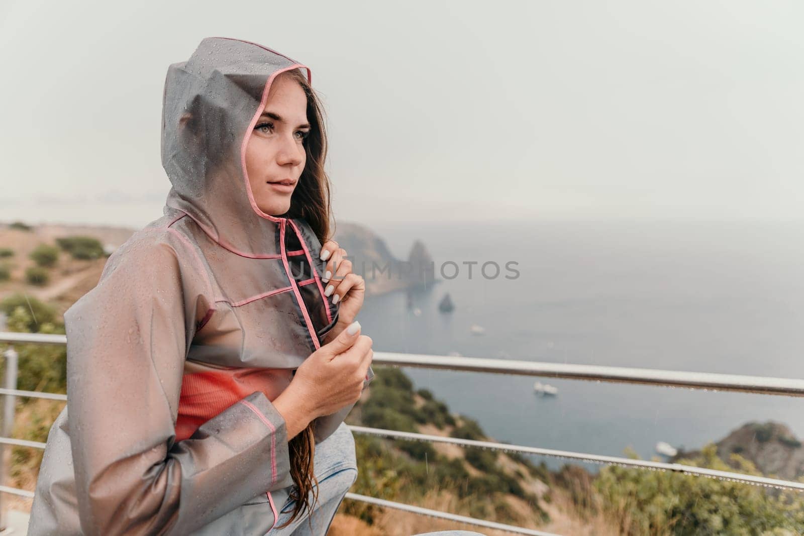 Woman rain park. Happy woman portrait wearing a raincoat with transparent umbrella outdoors on rainy day in park near sea. Girl on the nature on rainy overcast day