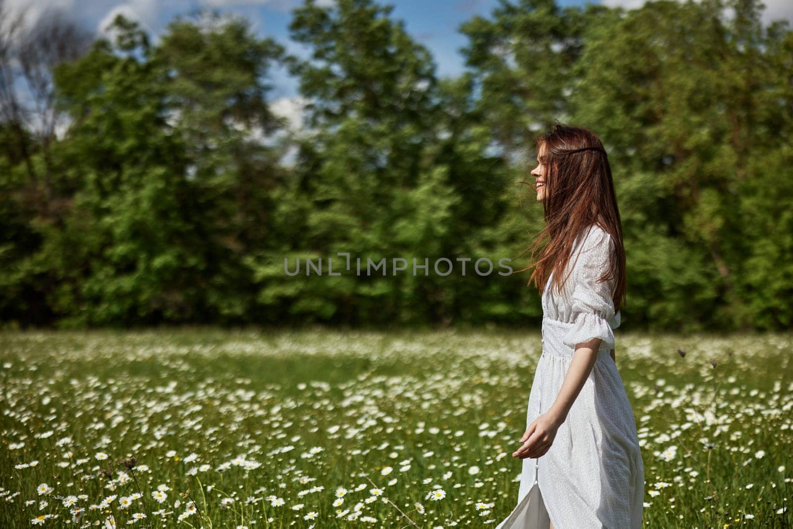 portrait of a free woman in a light dress in a chamomile field against the backdrop of hills enjoying nature. High quality photo