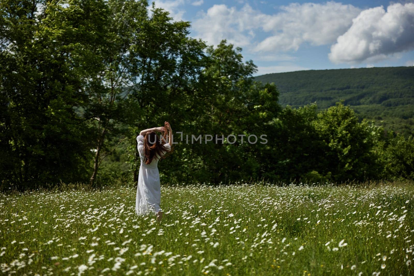 a woman in a light dress stands far away in a field of daisies with her back to the camera raising her hands to the sky. High quality photo