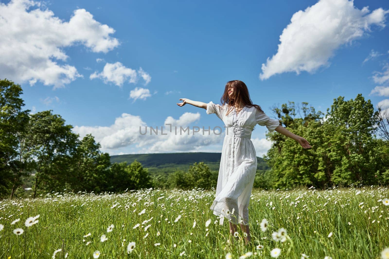 a woman in a long light dress with hair covering her face in a chamomile field against a blue sky with clouds by Vichizh