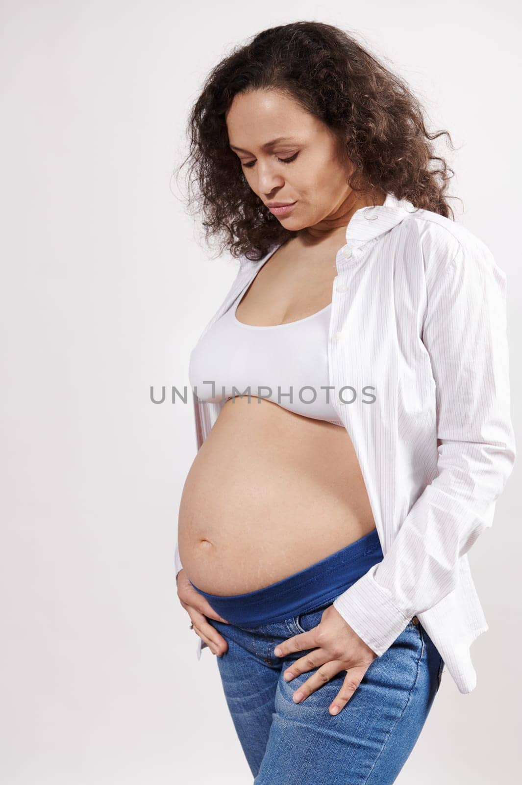 Attractive ethnic pregnant woman posing bare belly, isolated over white background. Pregnancy fashion. Body positivity by artgf