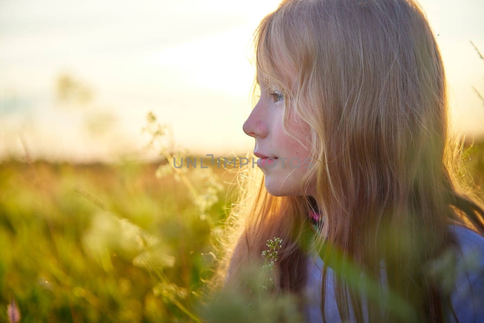 Portrait of pretty blonde girl having fun in a meadow on a natural landscape with grass and flowers on a sunny summer day. Portrait of a teenage child in summer or spring outdoors on field