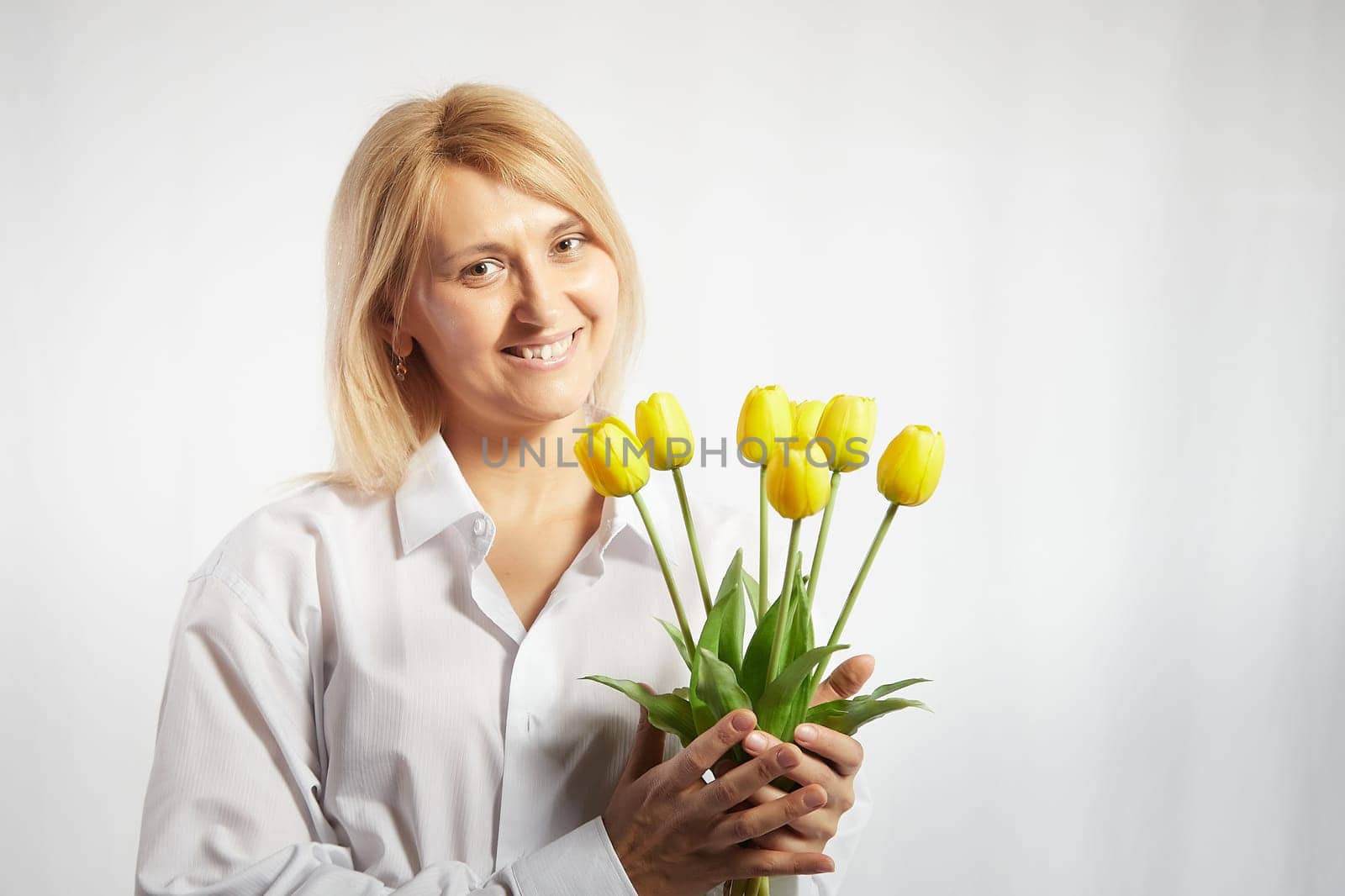 Beauty young blonde happy woman with bouquet of yellow tulips on white background. The concept of holiday and a gift for a lady and a girl. . Copy space