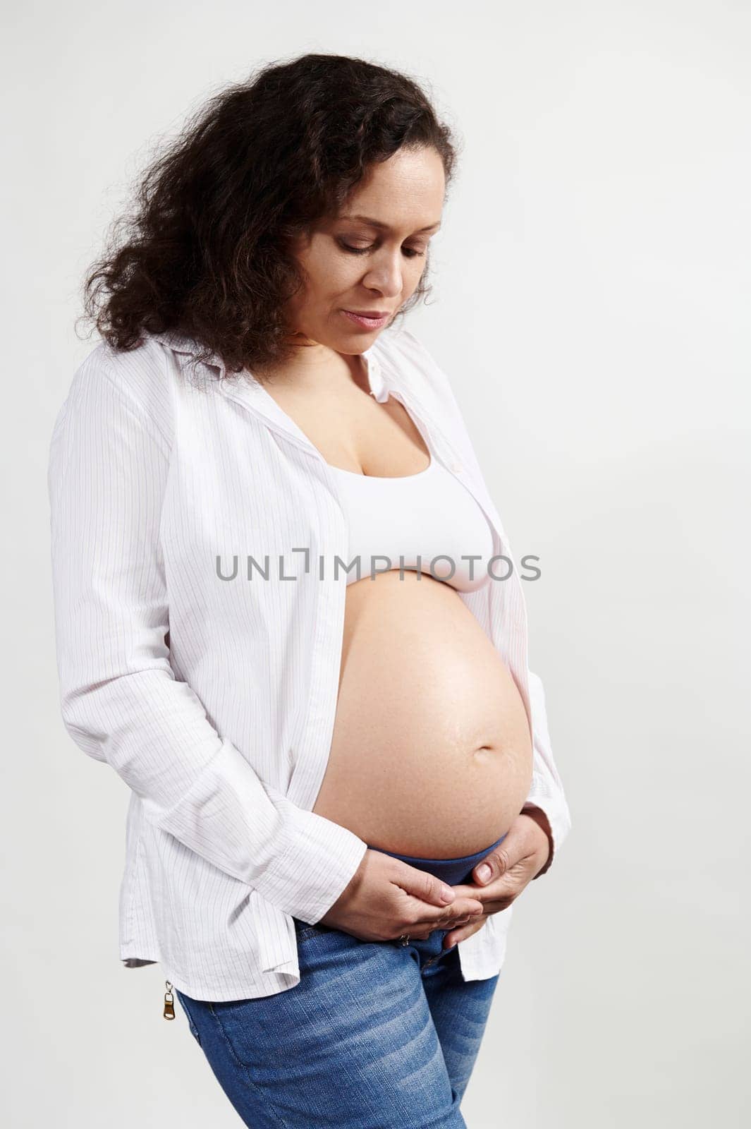 Confident serene delightful African American pregnant woman 30-39 years old, expecting a baby, touching belly over isolated white background. Pregnancy fashion. 6 month. 24 weeks. Maternity concept
