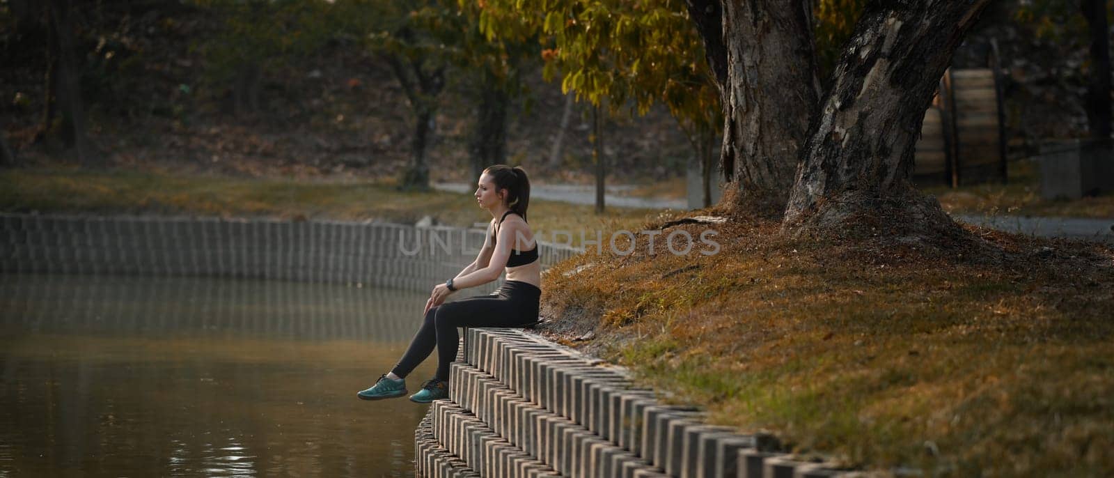 Image of athletic woman resting after workout session near river. Fitness, training and healthy lifestyle concept.