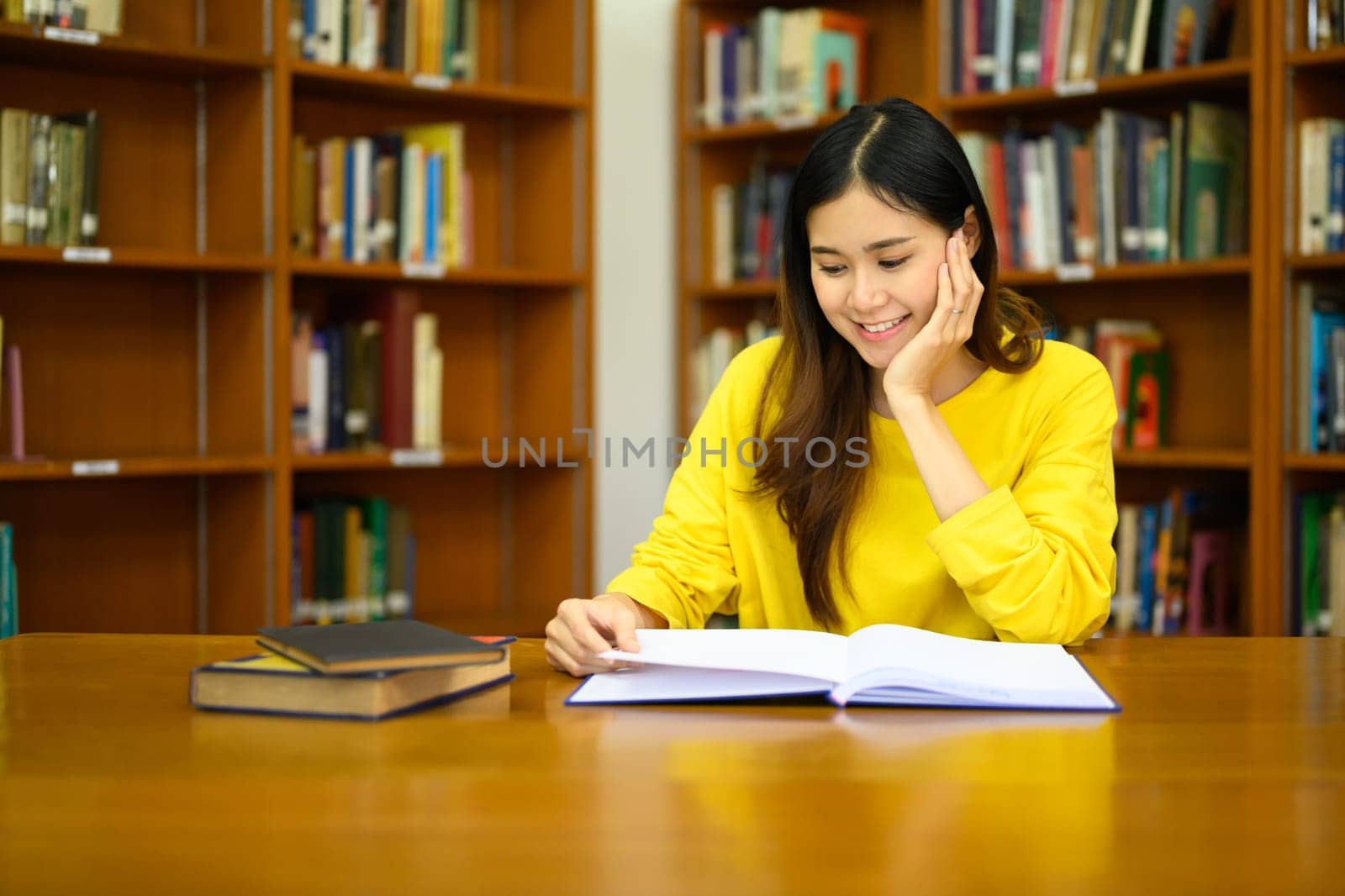 Portrait of attractive young woman reading book, preparing for exam in library. People, knowledge and education concept.