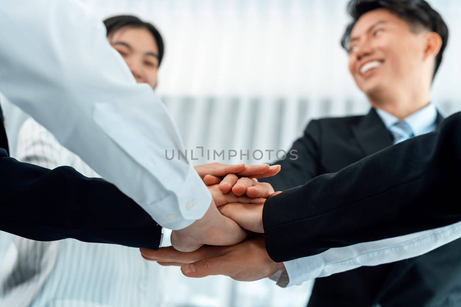 Bottom view partial hands wearing formal suit joining stack as symbol of team building, unity and harmony in office workplace. Successful business team of synergy holding hand together