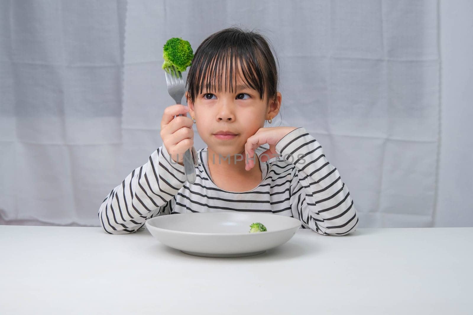 Children love to eat vegetables. Cute Asian girl eating healthy vegetables in her meal. Nutrition and healthy eating habits for children. by TEERASAK