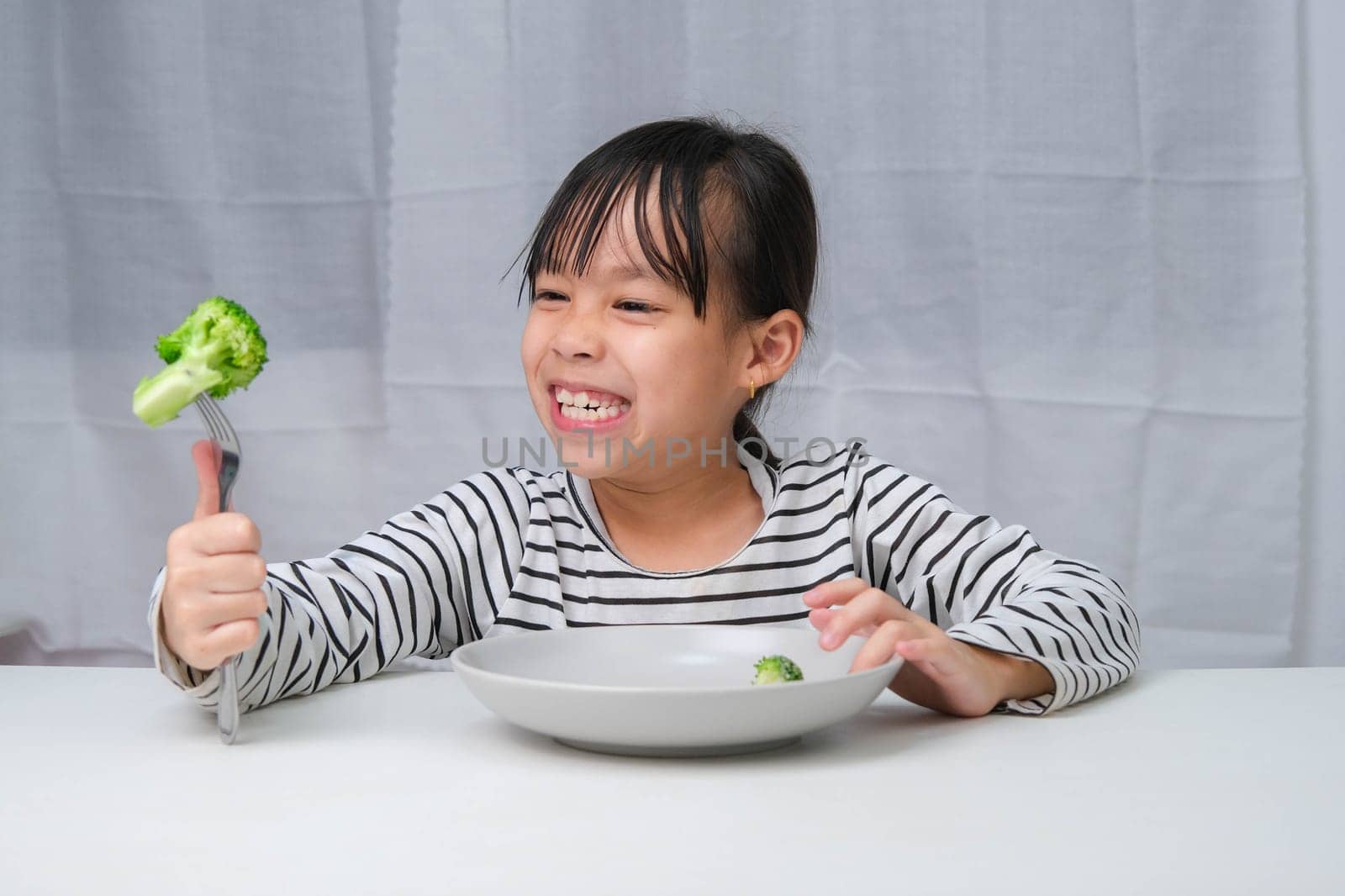Children love to eat vegetables. Cute Asian girl eating healthy vegetables in her meal. Nutrition and healthy eating habits for children. by TEERASAK