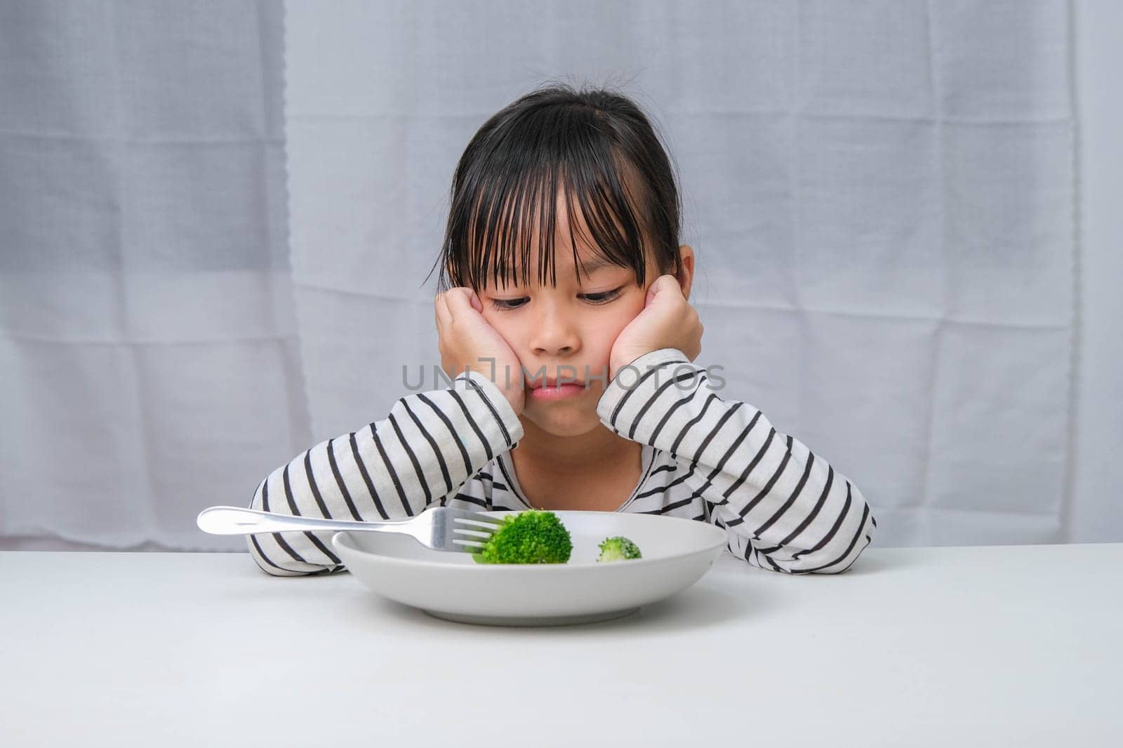 Children don't like to eat vegetables. Cute Asian girl refusing to eat healthy vegetables. Nutrition and healthy eating habits for children. by TEERASAK