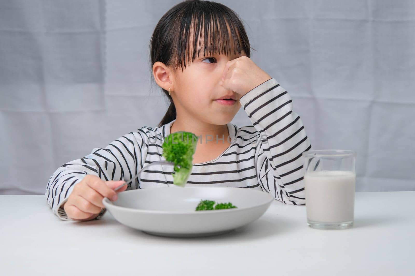 Children don't like to eat vegetables. Cute Asian girl refusing to eat healthy vegetables. Nutrition and healthy eating habits for children. by TEERASAK