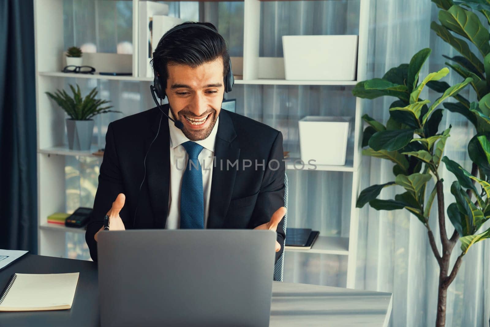 Male call center operator or telesales representative siting at his office desk wearing headset and in conversation with client providing customer service support or making persuasive sale. fervent