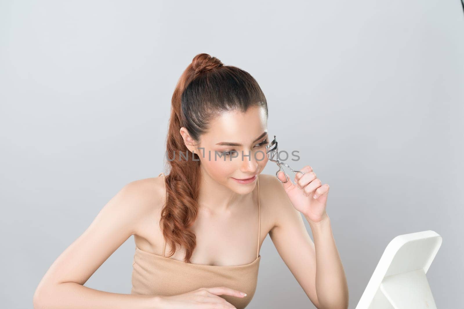 Glamorous facial makeup, beautiful woman with perfect smooth cosmetic clean skin correct eyelash curler with metal mechanic beauty accessory in isolated background.