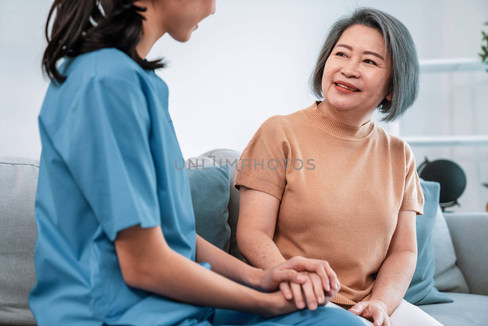 A contented senior woman visited by her personal caregiver and hold each other's hands.