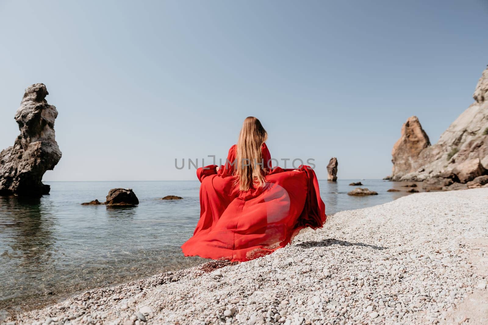 Woman travel sea. Happy tourist in red dress enjoy taking picture outdoors for memories. Woman traveler posing on the rock at sea bay surrounded by volcanic mountains, sharing travel adventure journey by panophotograph