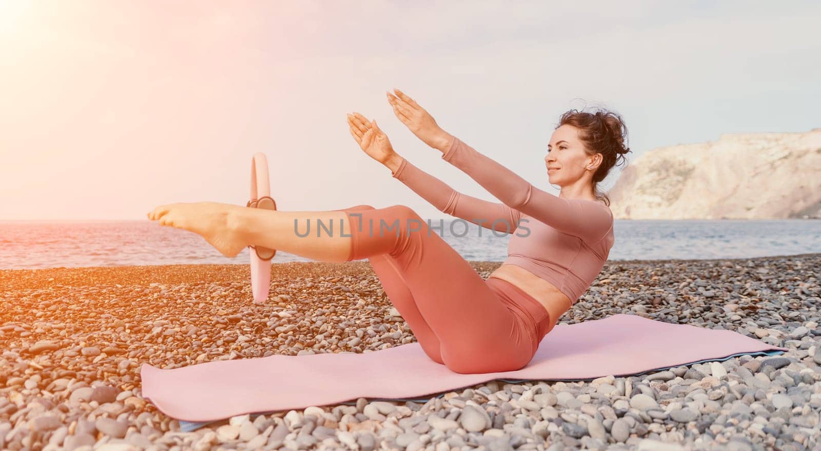 Woman sea pilates. Sporty happy middle aged woman practicing fitness on beach near sea, smiling active female training with ring on yoga mat outside, enjoying healthy lifestyle, harmony and meditation by panophotograph