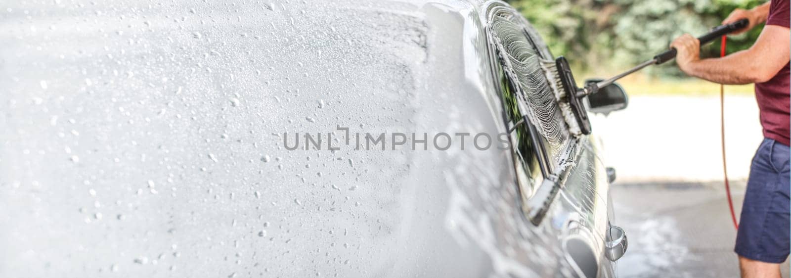 Man washing his car at self serve carwash, brush cleaning glass covered in shampoo. Left side is expanded to banner size, space for text.