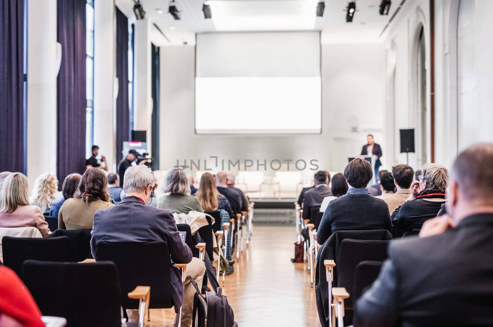 Speaker giving a talk in conference hall at business event. Rear view of unrecognizable people in audience at the conference hall. Business and entrepreneurship concept