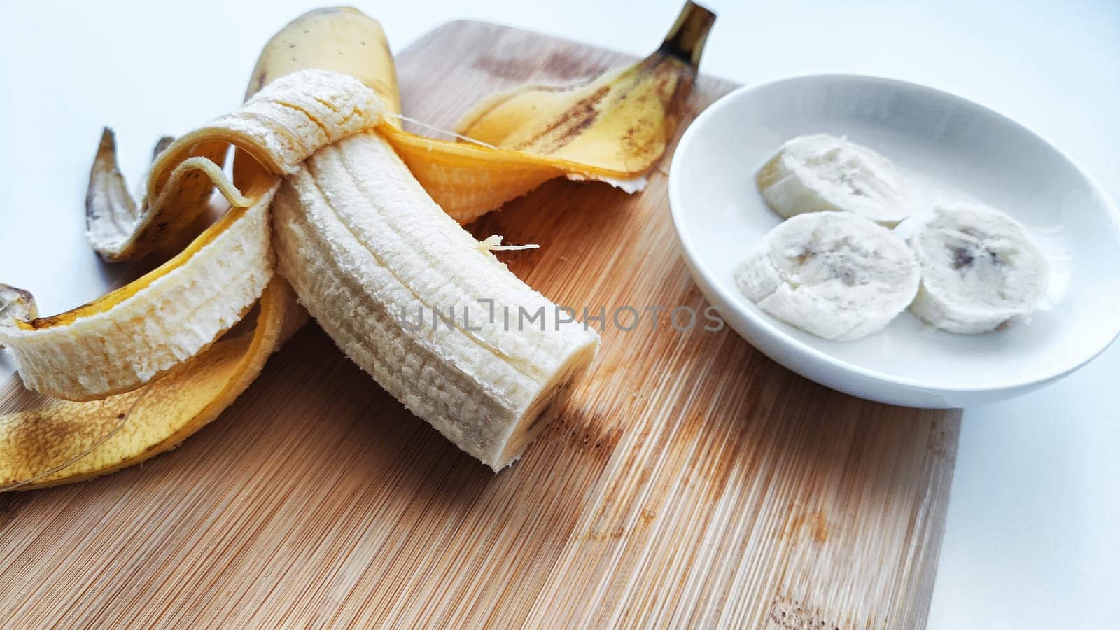 Banana with open panel on wooden board and sliced round pieces on the plate on white background. Ripe banana with peel and cooking. Delicious sweet fruit dessert. Close up