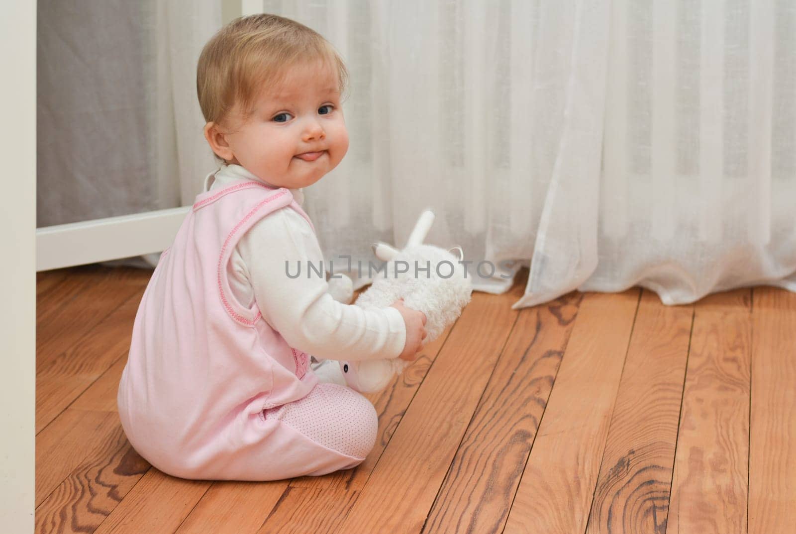 Little girl holding toy in hands and showing tongue