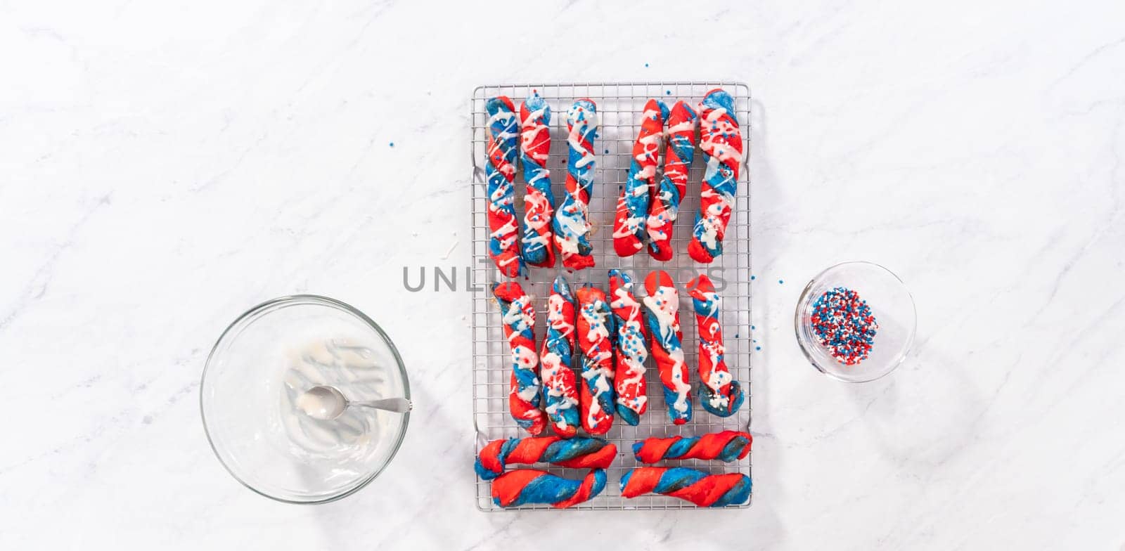 Flat lay. Drizzling white glaze on top of patriotic cinnamon twists. and decorating with star sprinkles.