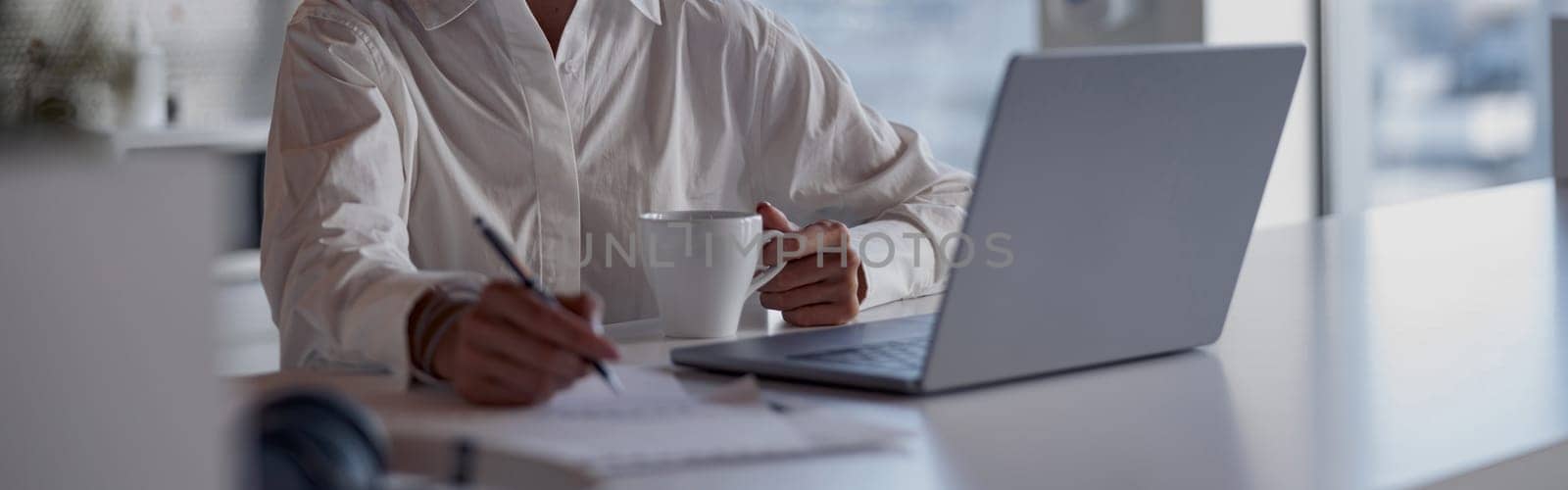 Charming businesswoman working at the office using a laptop looking away. Blurred background