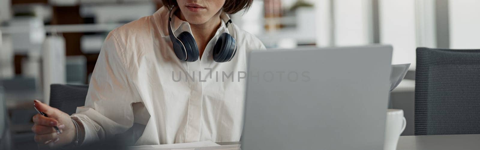 Business woman working laptop and making notes while sitting in modern office. Blurred background