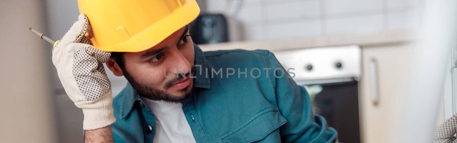 Male worker in uniform is assembling furniture on kitchen. Repair concept. High quality photo