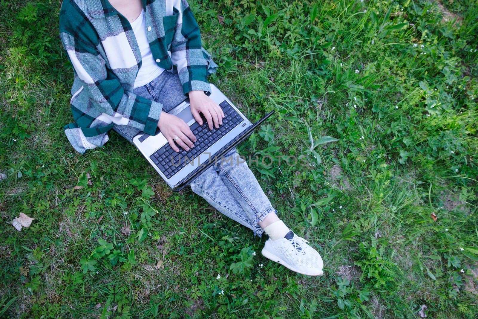 Top view of woman sitting in park on the green grass with laptop, notebook and smartphone, hands on keyboard. Student studying outdoors. download image